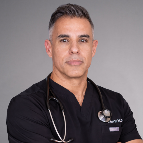 A professional portrait of a doctor wearing black scrubs and a stethoscope around his neck. His arms are crossed, and he has short, graying hair.